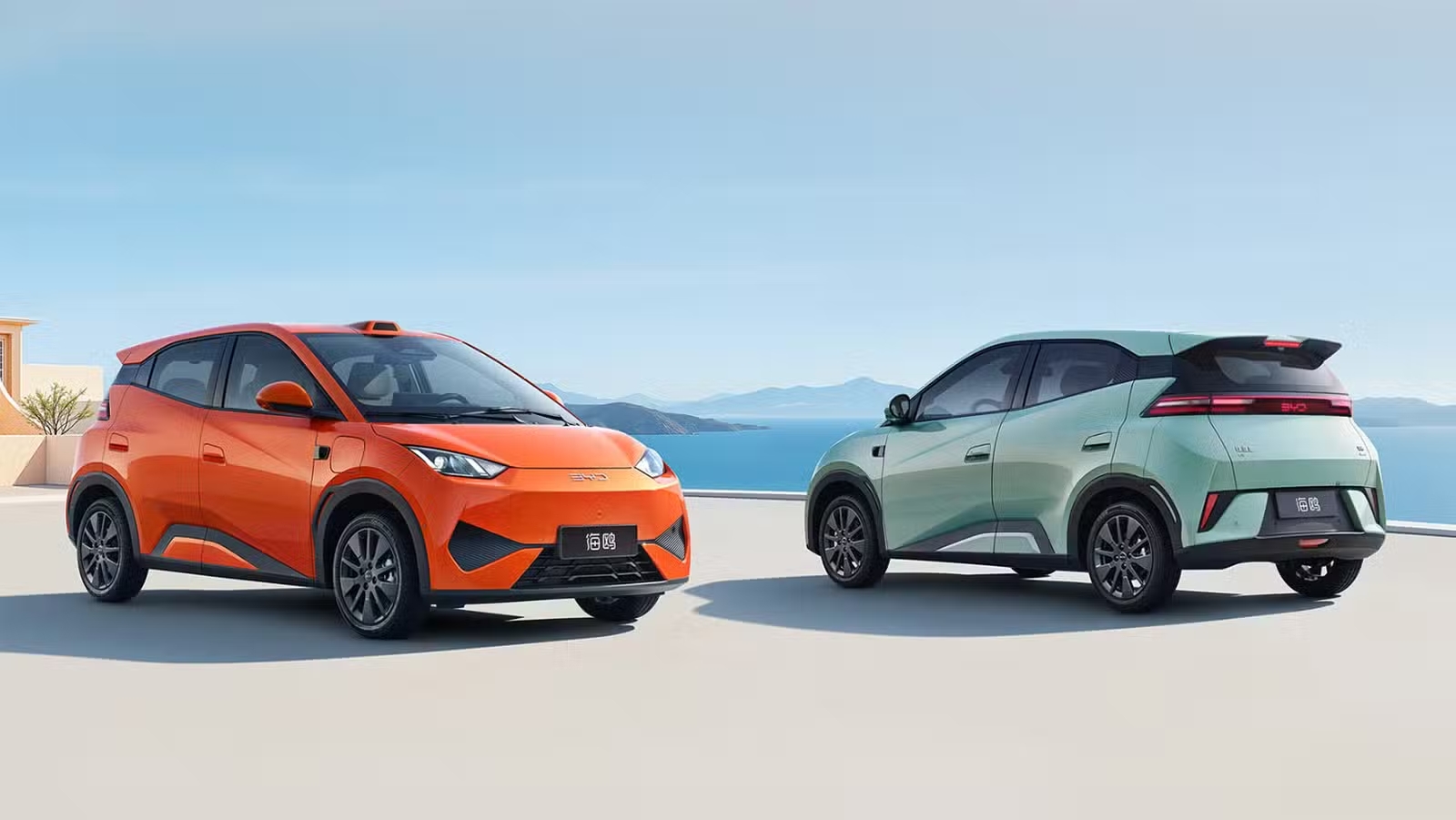Dois carros modernos, um laranja e um verde, em um cenário costeiro deslumbrante, destacam inovação e estilo.