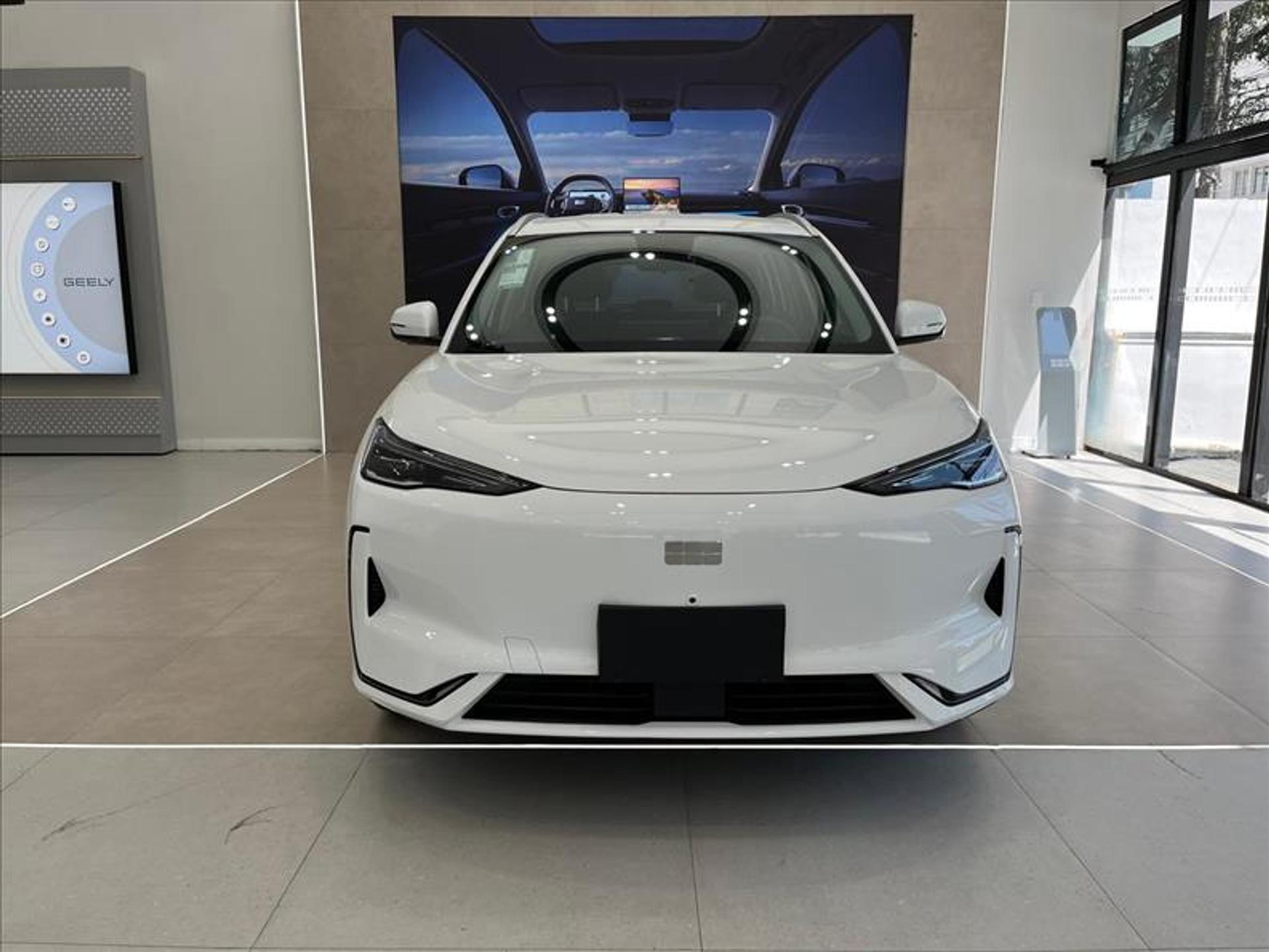 Automóvel elétrico branco em exposição, com interior moderno e painel digital ao fundo na concessionária Geely.