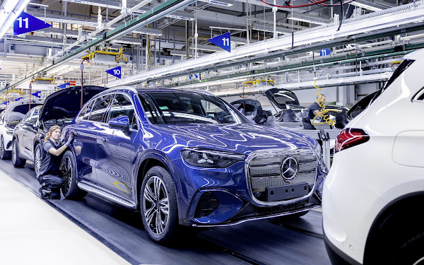 Carro SUV da Mercedes-Benz em uma linha de montagem, com um trabalhador realizando ajustes técnicos.